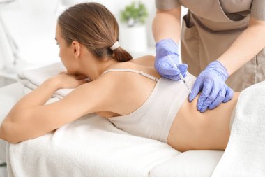 Kozmetik uzmanının ofisinde sırtına iğne batırılan genç bir kadın.