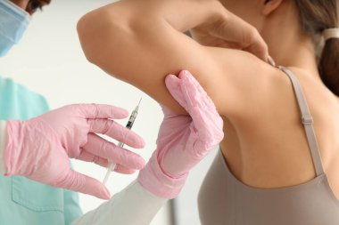 Kozmetik uzmanının ofisinde koluna iğne batırılan genç bir kadın.