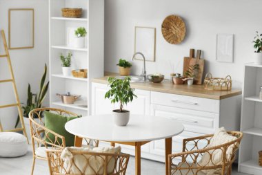 Beyaz tezgahları, yemek masası ve bitkileri olan aydınlık mutfağın içi.