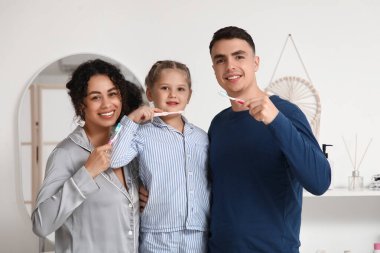 Küçük kız ve ailesi banyoda dişlerini fırçalıyorlar.