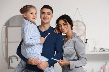 Küçük kız ve ailesi banyoda diş fırçası ve pijama giyiyorlar.
