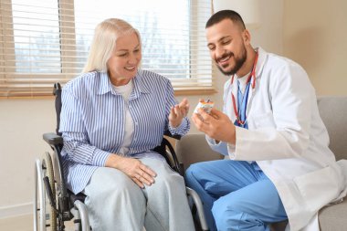 Evde glukometre kullanan, tekerlekli sandalyedeki olgun bir kadınla erkek doktor.