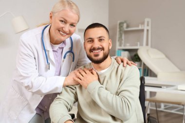 Kadın doktor hastanede tekerlekli sandalyedeki genç adama sarılıyor.