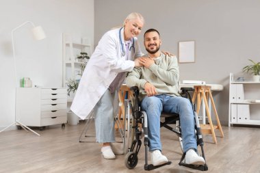 Kadın doktor hastanede tekerlekli sandalyedeki genç adama sarılıyor.