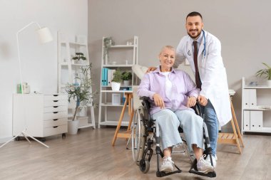 Hastanede tekerlekli sandalyede yetişkin bir kadınla erkek doktor.