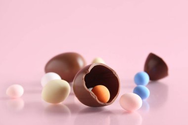 Tatlı çikolata yumurtaları ve pembe arka planda dağınık şekerler.
