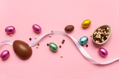 Alüminyum folyoda çikolatalı yumurta ve pembe arka planda kurdele.