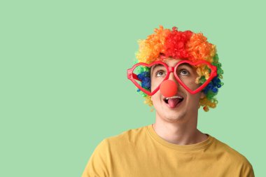 Yeşil arka planda palyaço kılığına girmiş genç adam, yakın plan.