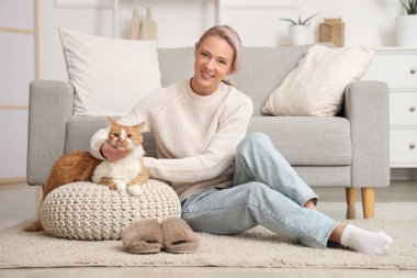 Pouf 'un üstünde kedisi ve evde yumuşak terlikleri olan güzel bir kadın.
