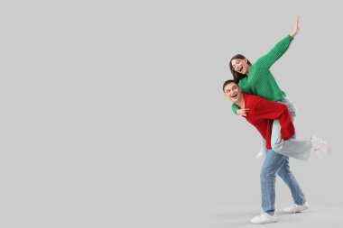 Gri arka planda hoş, genç bir çift, sıcak kazaklar giyip eğleniyorlar.