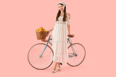 Pembe arka planda bisiklet ve bir sepet turtası olan genç bir kadın.