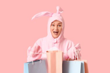 Paskalya tavşanı kostümlü, pembe arka planda alışveriş torbaları olan son sınıf öğrencisi bir kadın.