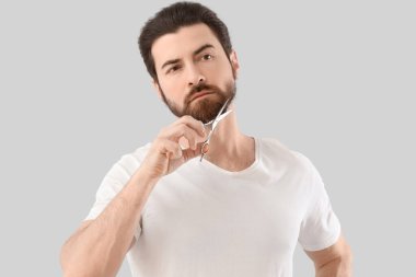 Yakışıklı genç adam, sakalını gri arka planda makasla süsledi.