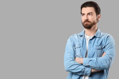 Gri arka planda çapraz kollu sakallı genç adam.