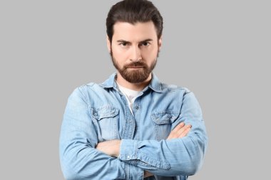 Gri arka planda çapraz kollu sakallı genç adam.