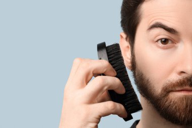 Yakışıklı genç adam mavi arka planda sakalını fırçalıyor, yakın plan.