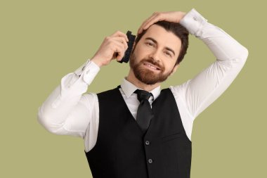 Sakallı genç adam yeşil arka planda sakalını fırçalıyor.