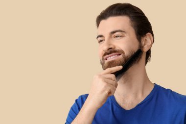 Sakalını bej arka planda tarayan yakışıklı genç adam.