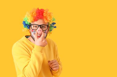 Palyaço kılığına girmiş, sarı arka planda domuz burunlu genç adam.