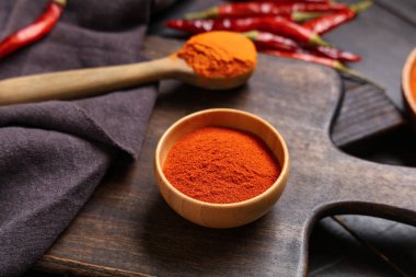 Ahşap zemin üzerinde kırmızı biber tozu olan kase ve kaşık, yakın plan.