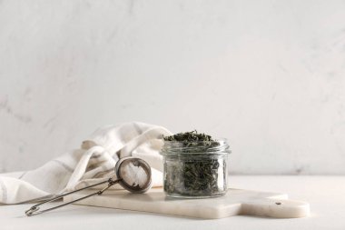 Kurumuş yeşil çay yapraklı kavanoz ve beyaz arka planda süzgeç.