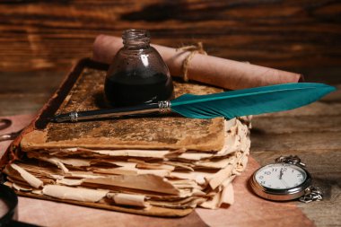 Ahşap zemin üzerinde kalem, mürekkep, parşömen ve cep saati olan eski bir kitap.