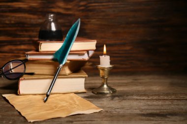 Ahşap zemin üzerinde kalem, mürekkep hokkası, mum ve kağıt çarşaf olan eski kitaplar.