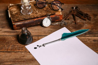 Kağıt çarşaf, tükenmez kalem, mürekkep hokkası, gözlük ve ahşap arka planda cep saati olan eski kitap.