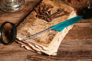 Ağaç zemin üzerinde kalem, büyüteç ve anahtarlar olan eski bir kitap.