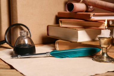 Ağaç zemin üzerinde kalem, mürekkep hokkası, büyüteç ve parşömen bulunan kitaplar