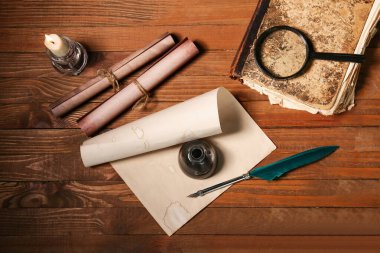 Kağıt çarşaf, tükenmez kalem, mürekkep hokkası, büyüteç ve tahta zemin üzerinde parşömenler olan eski bir kitap.