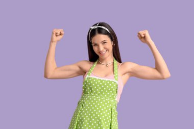 Önlüklü genç kadın leylak arka planda kaslarını gösteriyor. Kadın Tarihi Ayı