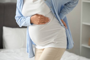 Genç hamile kadın yatak odasında sırt ağrısı çekiyor, yakın plan.