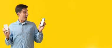 Sarı arka planda cep telefonu ve güç bankasını tutan genç adam şaşırdı.