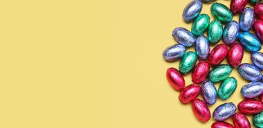 Birçok çikolatalı Paskalya yumurtası bej arka planda, yazı için yeri ve üst görünümü olan folyoda.