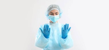 Kadın cerrah, hafif arka planda lastik eldivenlerle ellerine bakıyor.