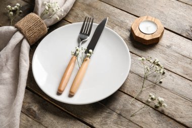 Kahverengi ahşap arka planda katlanmış peçete, çatal bıçak ve mum tabağı.