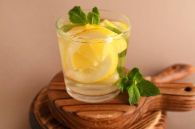 Kahverengi zemin üzerinde limon ve nane aromalı bir bardak erimiş su.