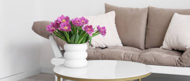 Aydınlık oturma odasındaki masada taze lalelerle vazo.