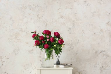 Şakayık, dergi ve aroma çubukları olan vazo bej rengi grunge duvarın yanındaki sehpanın üzerinde.