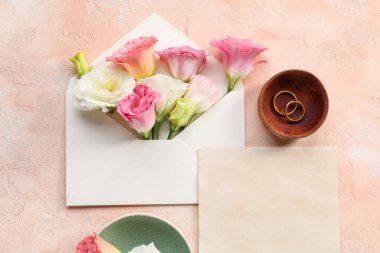 İçinde boş kart, zarf, alyans ve bej arka planda güzel Eustoma çiçekleri olan kompozisyon, yakın plan.