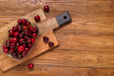 Ahşap zemin üzerinde taze kiraz olan plastik bir kap.