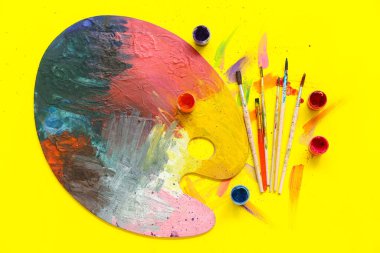 Sanatçı fırçaları, paletler ve sarı arkaplanda boyalar
