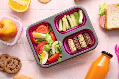 Beslenme çantalarında lezzetli yiyecekler ve pembe fayansların üzerinde bir şişe meyve suyu.