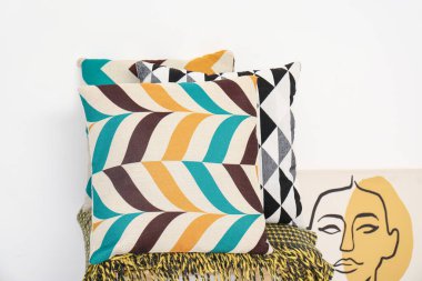 Battaniye ve yastıklar beyaz duvarın yanındaki taburede, yakın plan.