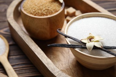 Aromatik vanilya şekerli kaseler, çiçek ve tahta arka planda sopalar.