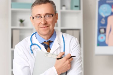 Tıbbî ofiste panosu olan olgun bir doktor, yakın plan.