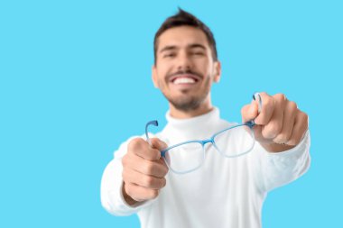 Mavi arka planda gözlüklü genç adam, yakın plan.