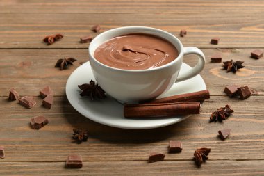 Bir fincan lezzetli eritilmiş çikolata, tarçın çubukları ve ahşap arka planda yıldız anason.