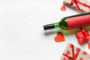 Hediye kutularıyla dolu bir şişe şarap ve beyaz arka planda kağıt kalpler. Sevgililer Günü kutlaması